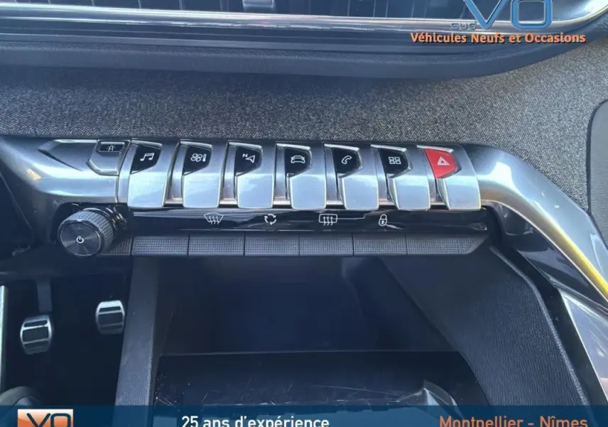 Gros plan sur la rangée de commandes chromées du tableau de bord du Peugeot 3008 gris foncé, avec pédales visibles en dessous.