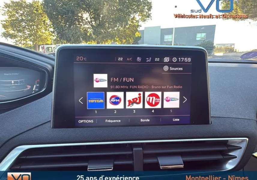 Vue intérieure centrée sur l'écran tactile du Peugeot 3008 gris foncé, affichant les stations radio FM avec tableau de bord en arrière-plan.