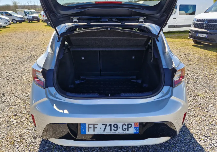 Vue arrière ouverte sur le coffre d'une Toyota Corolla hybride gris clair métal, montrant l'espace de chargement vide.