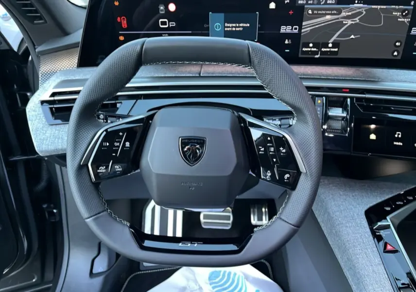 Vue rapprochée du volant cuir multifonctions Peugeot 5008 Hybrid 145 GT Alcantara avec tableau de bord numérique et finition grise.