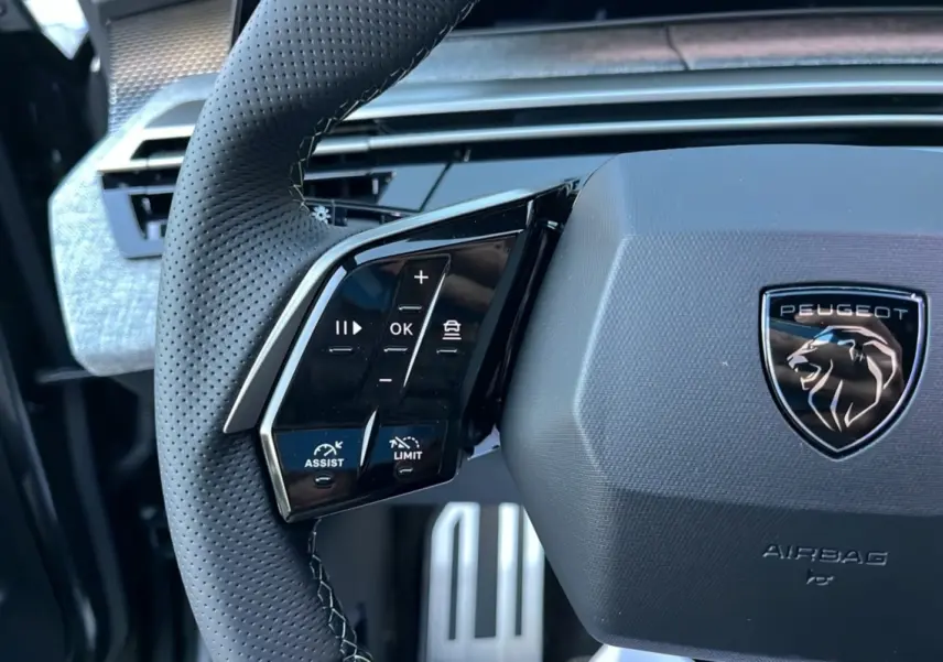 Gros plan sur le volant cuir perforé du Peugeot 5008 Hybrid 2025, avec commandes multifonctions et logo lion noir.