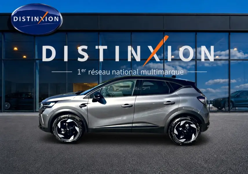 Profil côté gauche du Renault Captur gris cassiopée 2026 devant une vitrine avec logo Distinxion.