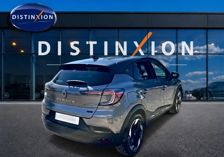 Vue 3/4 arrière droite du Renault Captur gris cassiopée devant une vitrine avec logo Distinxion.