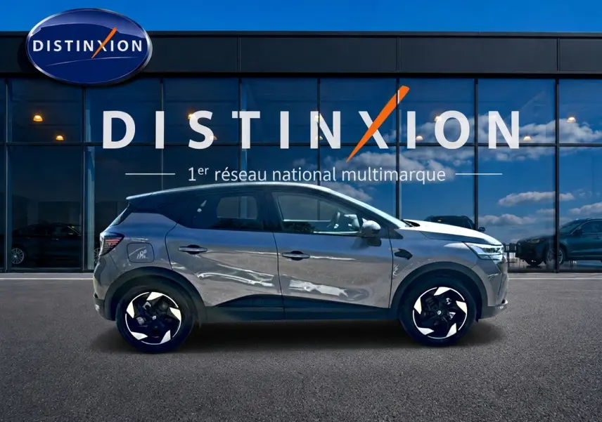 Renault Captur gris cassiopée en profil droit devant une vitrine avec logo Distinxion, jantes alu noires et blanches.