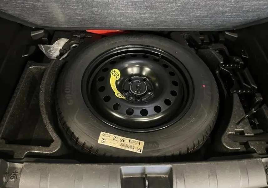 Roue de secours temporaire noire dans le coffre du Jeep Renegade gris 2024, avec plancher modulable visible.