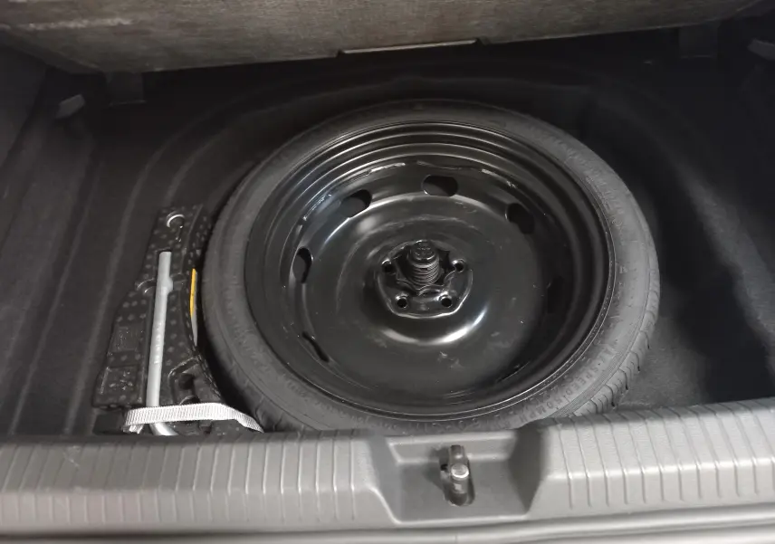 Roue de secours noire et cric dans le coffre d'une Volkswagen Golf 1.5 TSI gris dauphin, vue plongeante.