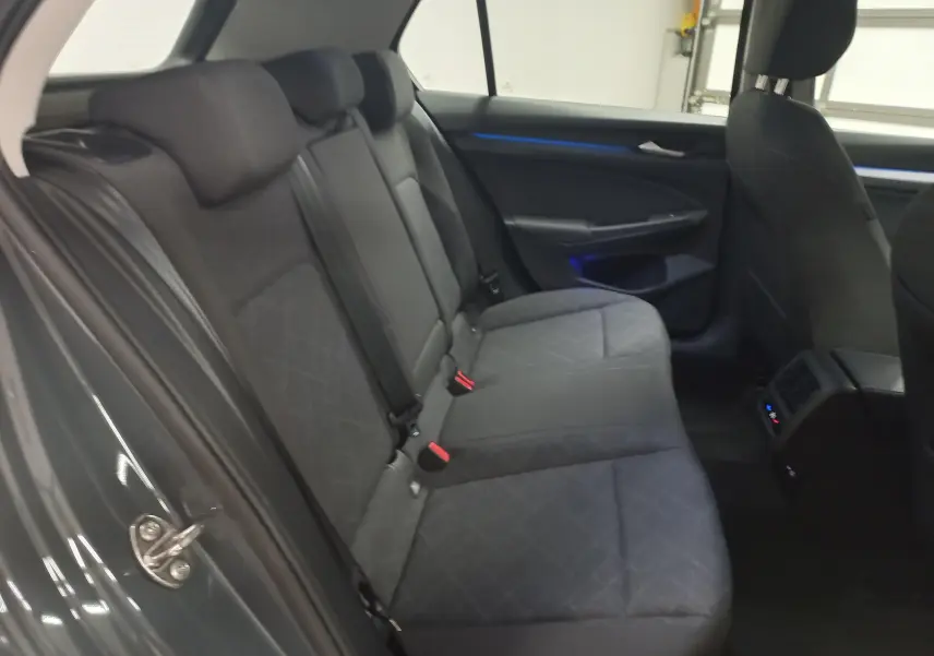Vue intérieure arrière côté gauche montrant les sièges arrière en tissu gris et l'éclairage d'ambiance bleu de la Volkswagen Golf 2023.