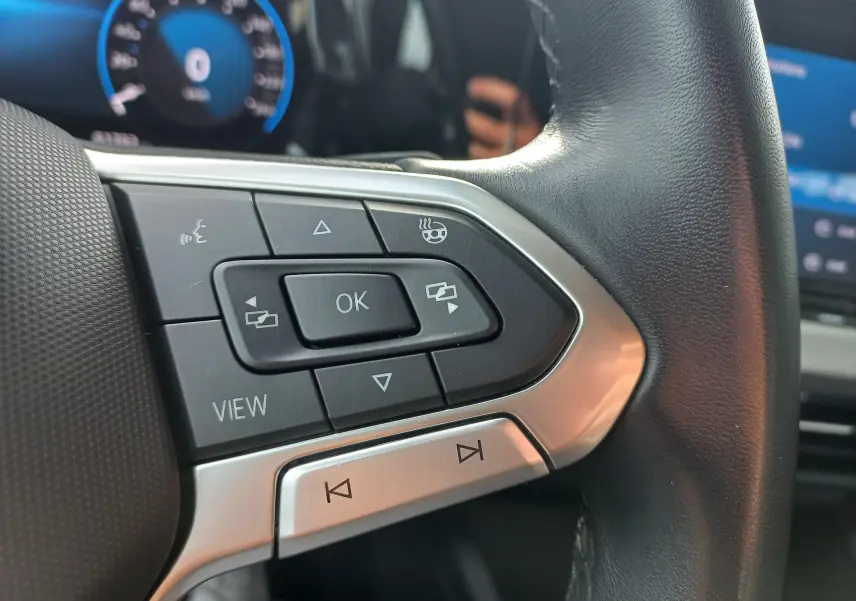 Gros plan sur les commandes du volant noir de la Volkswagen Golf 1.5 TSI 130 DSG7 Life Plus 2023, avec tableau de bord numérique bleu.