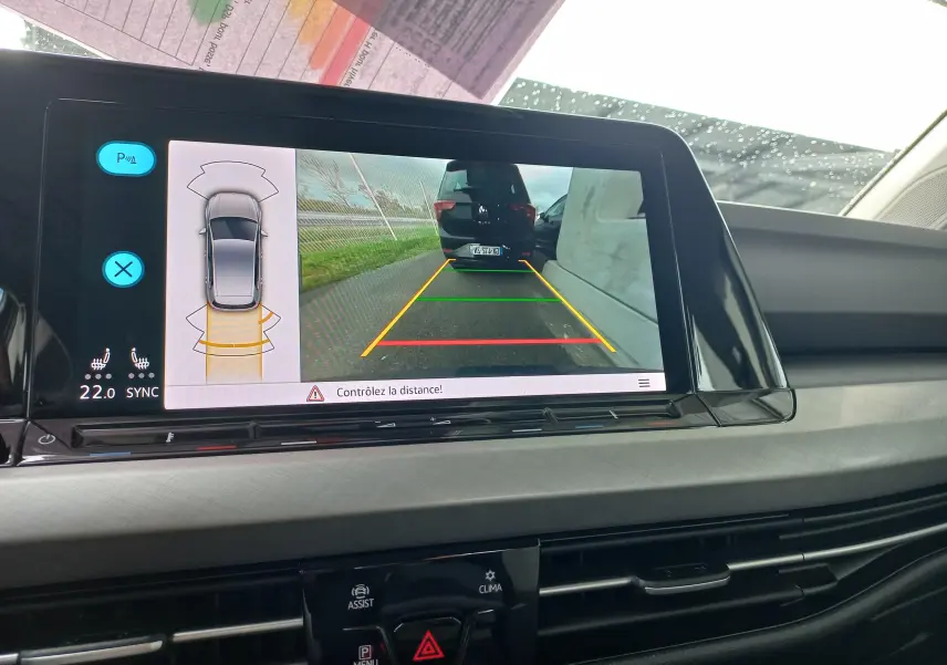 Écran intérieur affichant la caméra de recul d'une Volkswagen Golf gris dauphin avec lignes d'aide au stationnement.