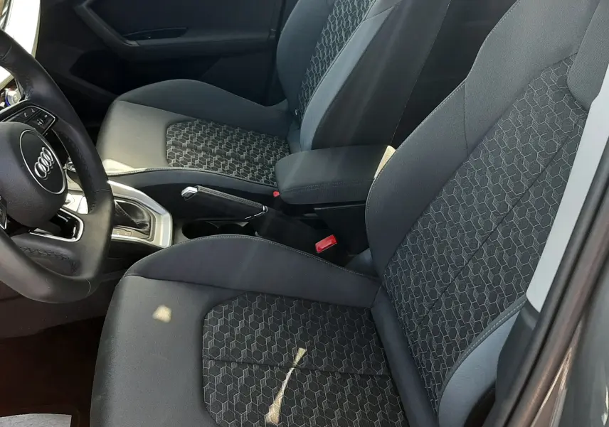 Vue intérieure côté conducteur de l'Audi A1 Sportback 2025, sièges tissu gris noir avec motifs hexagonaux et volant cuir.