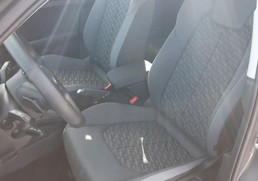 Vue intérieure côté conducteur de l'Audi A1 Sportback 2025, sièges tissu gris avec motifs hexagonaux et volant cuir sport.