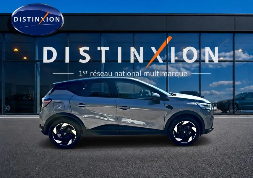 Renault Captur gris cassiopée en profil droit, avec jantes noires et toit noir, devant une vitrine Distinxion.