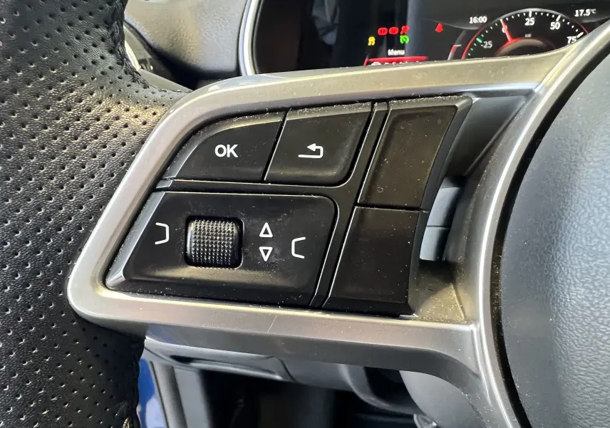 Gros plan sur les commandes gauche du volant perforé du SERES 3 Electric 163ch Luxe, tableau de bord partiellement visible.