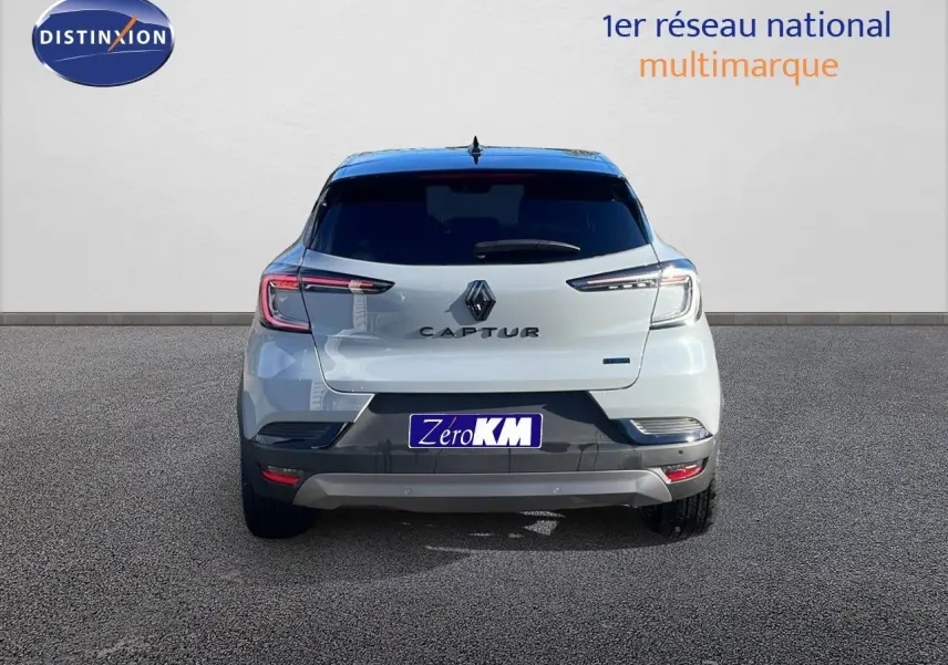 Vue arrière d'un Renault Captur E-Tech hybride gris Rafale avec toit noir, en stationnement sur sol gris.