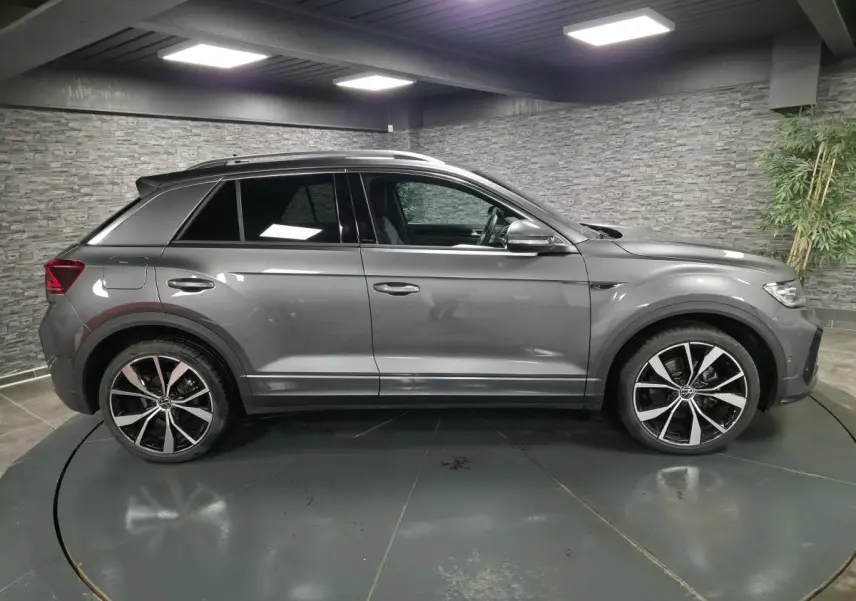 Vue de profil côté gauche d'un Volkswagen T-Roc gris métallisé avec jantes alliage 19 pouces et finitions R-Line.