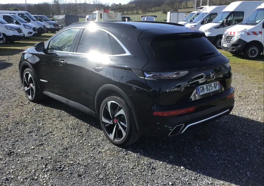 Vue 3/4 arrière droite d’un DS7 Crossback noir brillant avec jantes noires et détails chromés sous un ciel ensoleillé.
