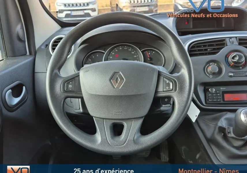 Vue intérieure centrée sur le volant Renault du Kangoo blanc 2016 avec tableau de bord et levier de vitesse manuel visibles.