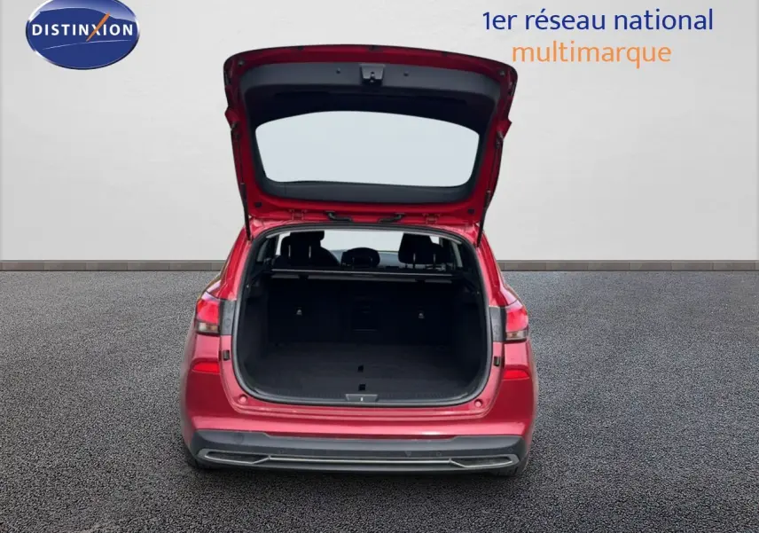 Vue arrière d'une Hyundai i30 SW 2023 rouge Sunset Red Metal avec coffre ouvert sur sol bitumé.