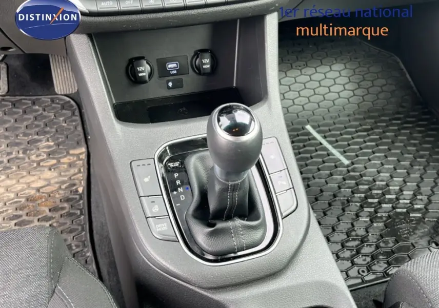 Vue rapprochée de la console centrale de la Hyundai i30 SW 2023, avec levier de boîte automatique et tapis caoutchouc noir.