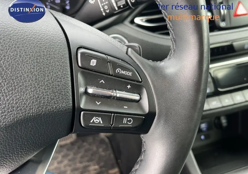 Gros plan sur le volant côté gauche du Hyundai i30 SW 2023 avec commandes multifonctions en plastique noir.