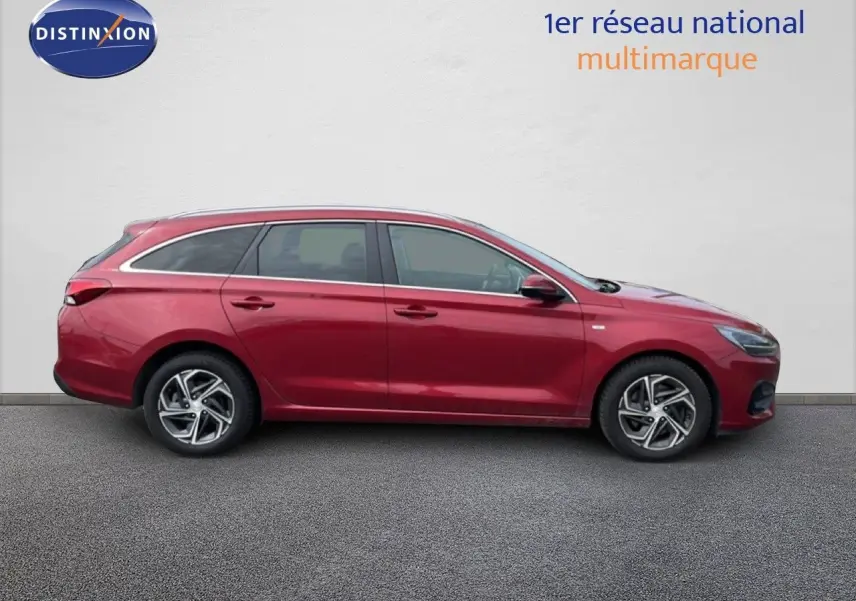 Profil latéral droit d'une Hyundai i30 SW 2023 rouge Sunset Red Metal avec jantes alliage bicolores.