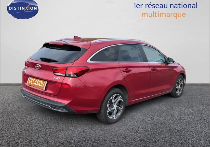 Vue 3/4 arrière droite d'une Hyundai i30 SW 2023 rouge Sunset Red Metal avec jantes alliage bicolores et vitres teintées.
