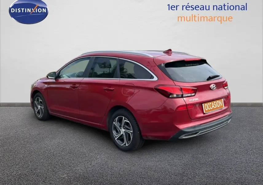 Vue 3/4 arrière droite d'une Hyundai i30 SW 2023 en rouge Sunset Metal avec jantes bi-ton et feux LED distinctifs.