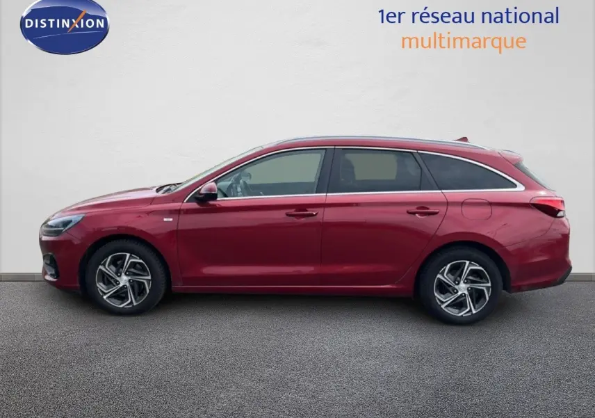 Vue de profil côté gauche d'une Hyundai i30 SW 2023 rouge Sunset Red Metal avec jantes alliage bi-ton.
