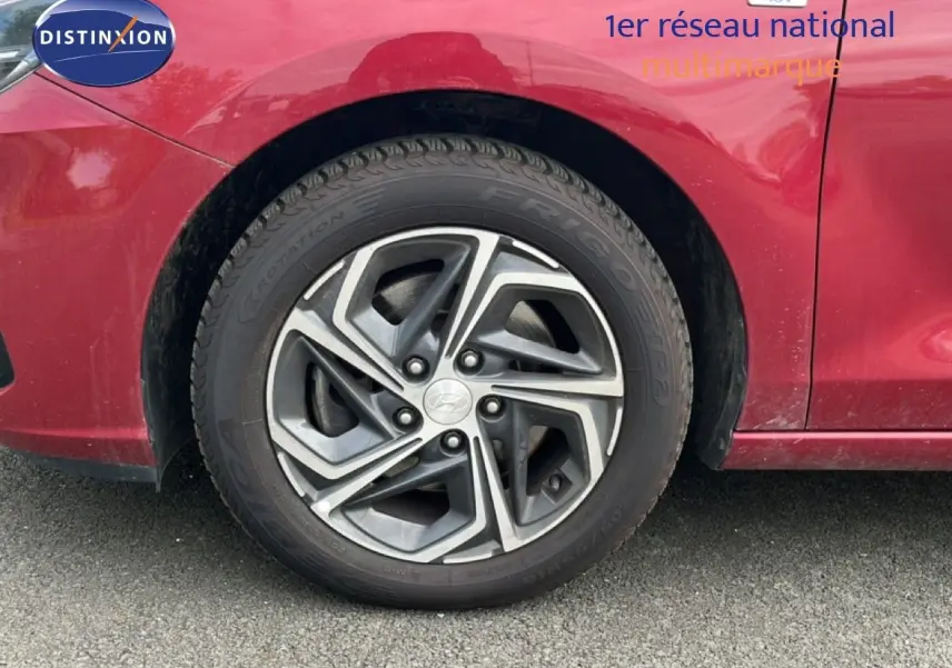 Gros plan sur la roue avant gauche d'une Hyundai i30 SW 2023 en rouge Sunset Metal avec jante alliage bicolore.