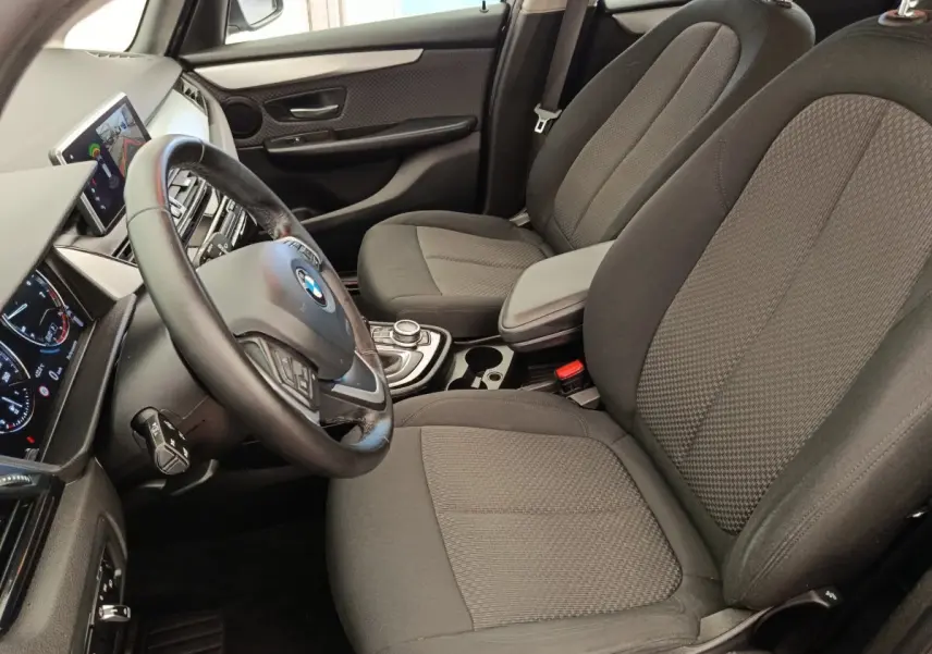 Vue intérieure côté conducteur de la BMW Série 2 Gran Tourer 218i Lounge 2022, sièges tissu gris et volant cuir multifonctions.