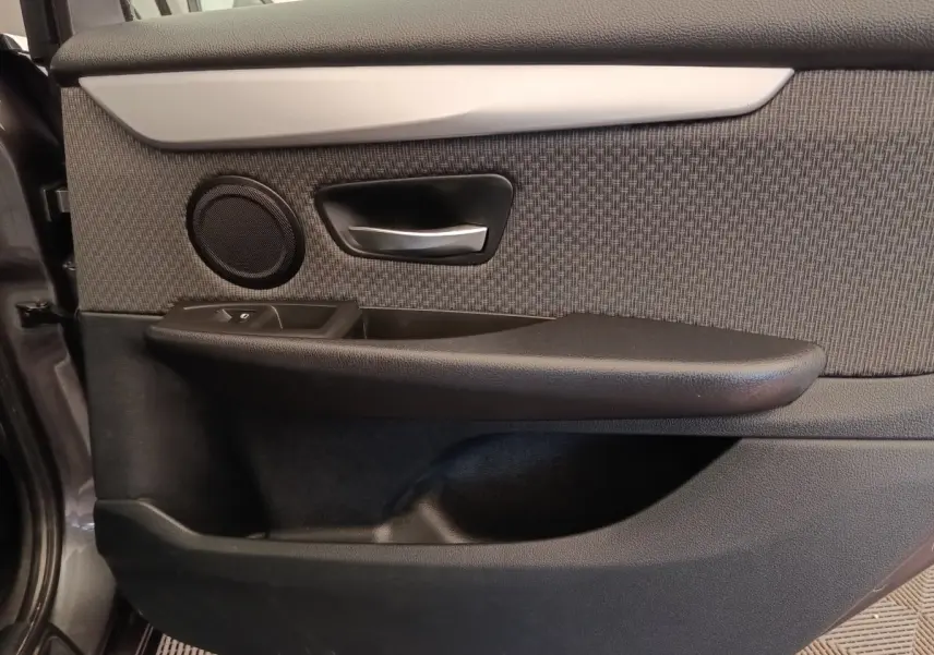Gros plan sur la porte intérieure côté conducteur de la BMW Série 2 Gran Tourer gris clair, avec poignée alu et haut-parleur intégré.