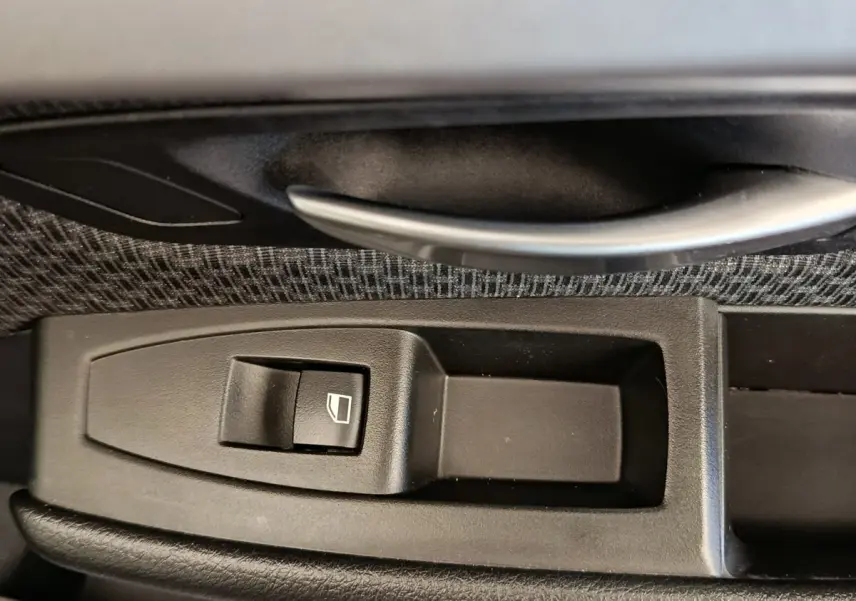 Gros plan sur la commande de lève-vitre côté conducteur avec poignée alu, intérieur tissu gris de la BMW Série 2 Gran Tourer 218i Lounge.