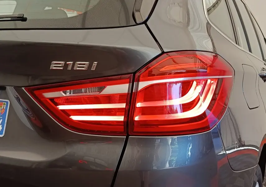 Gros plan sur le feu arrière droit allumé d'une BMW Série 2 Gran Tourer 218i gris clair, avec logo 218i visible.