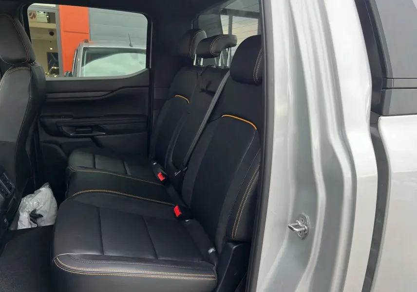 Vue latérale intérieure des sièges arrière noirs avec surpiqûres orange du Ford Ranger 2025 gris iconic version Wildtrak X Pack X Rideau.