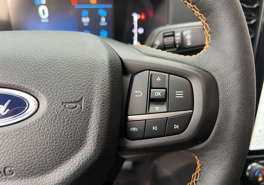 Gros plan sur le volant cuir noir avec surpiqûres orange du Ford Ranger 2025, boutons multifonctions visibles.