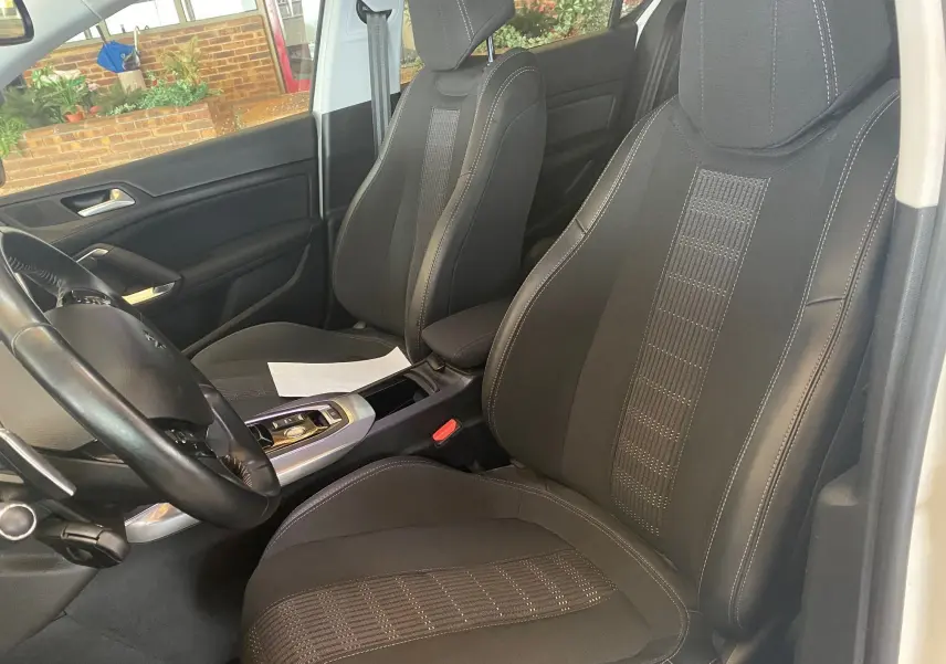 Vue intérieure côté conducteur de la Peugeot 308 blanche de 2020, sièges tissu noir avec coutures contrastées.