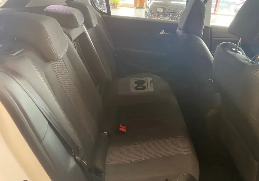 Vue intérieure des sièges arrière en tissu noir de la Peugeot 308 blanche, avec accoudoir central et porte-gobelets.