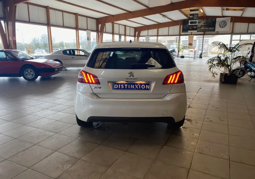 Vue arrière d'une Peugeot 308 blanche de 2020 avec feux arrière allumés dans un showroom lumineux.