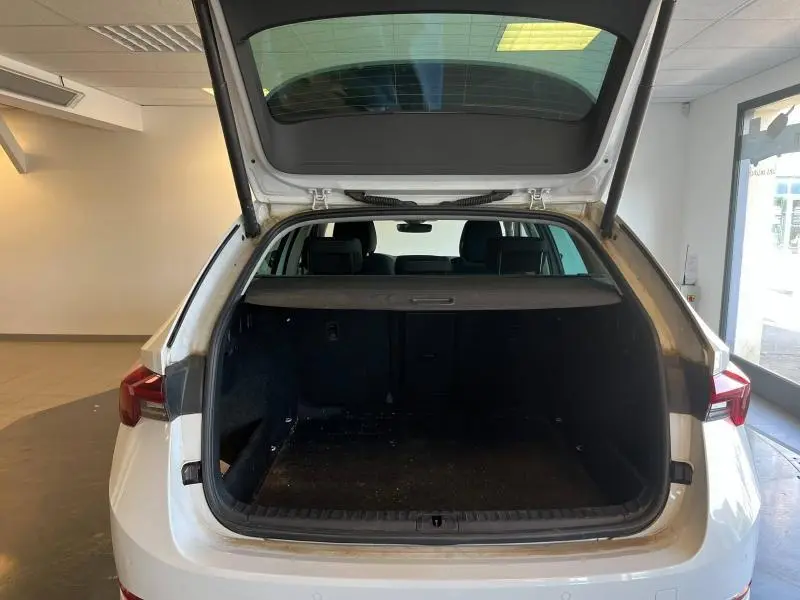 Vue arrière ouverte du coffre d'un SKODA OCTAVIA COMBI blanc cristal, montrant l'espace de chargement intérieur et la plage arrière.