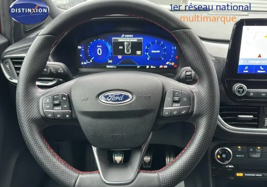 Vue rapprochée du volant perforé avec surpiqûres rouges et tableau de bord numérique de la Ford Puma rouge 2020.