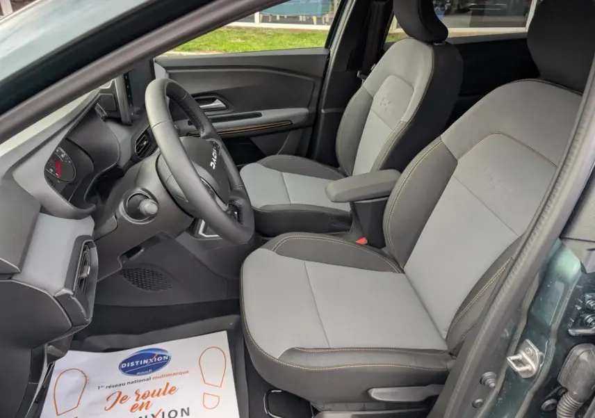 Vue intérieure côté conducteur du Dacia Jogger vert métallisé, montrant les sièges avant gris clair avec surpiqûres brunes.