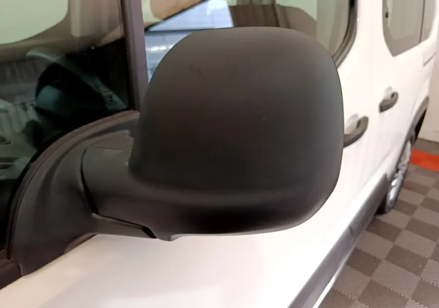 Rétroviseur noir côté conducteur d'un Peugeot Rifter blanc 2019, vue rapprochée sur la portière avant.
