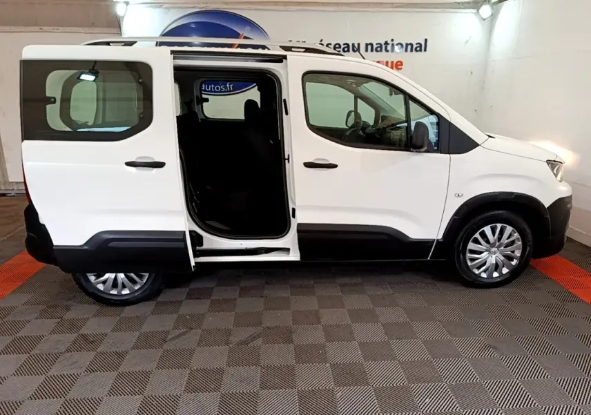 Vue de profil côté droit d'un Peugeot Rifter blanc 2019 avec porte coulissante arrière ouverte, intérieur sombre visible.