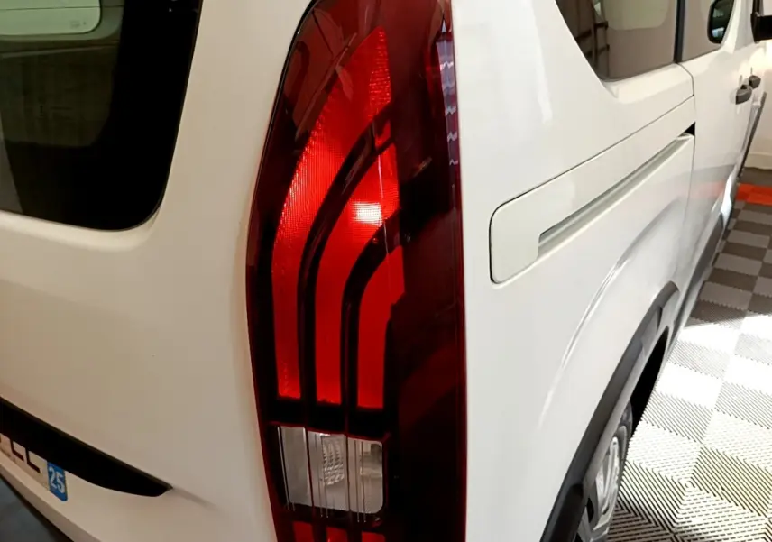 Gros plan sur le feu arrière droit rouge du Peugeot Rifter blanc, avec partie latérale et roue visible en intérieur.