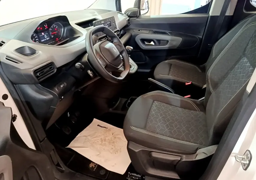Vue intérieure côté conducteur du Peugeot Rifter blanc 2019, montrant le tableau de bord et les sièges avant en tissu gris.