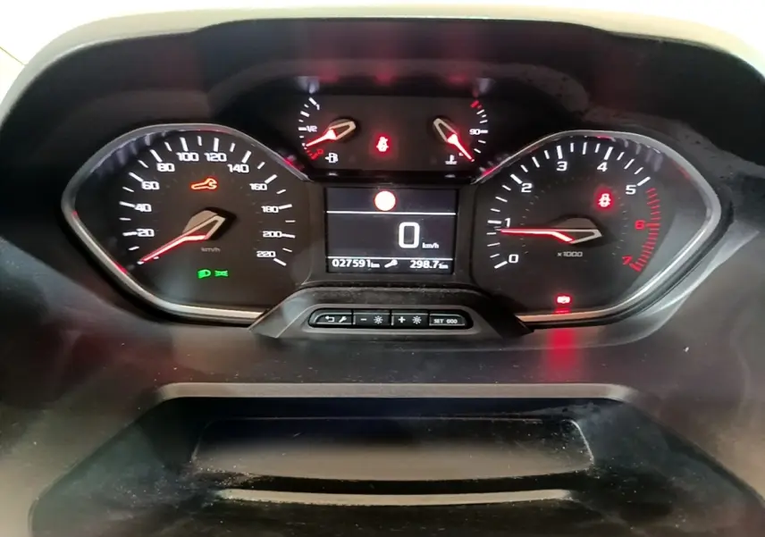 Vue rapprochée du tableau de bord numérique du Peugeot Rifter blanc, affichant la vitesse à 0 km/h et divers voyants allumés.