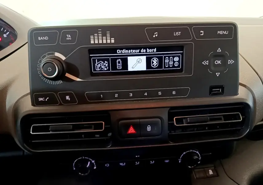 Vue rapprochée du tableau de bord noir du Peugeot Rifter blanc 2019, affichage multi-fonctions et commandes centrales visibles.