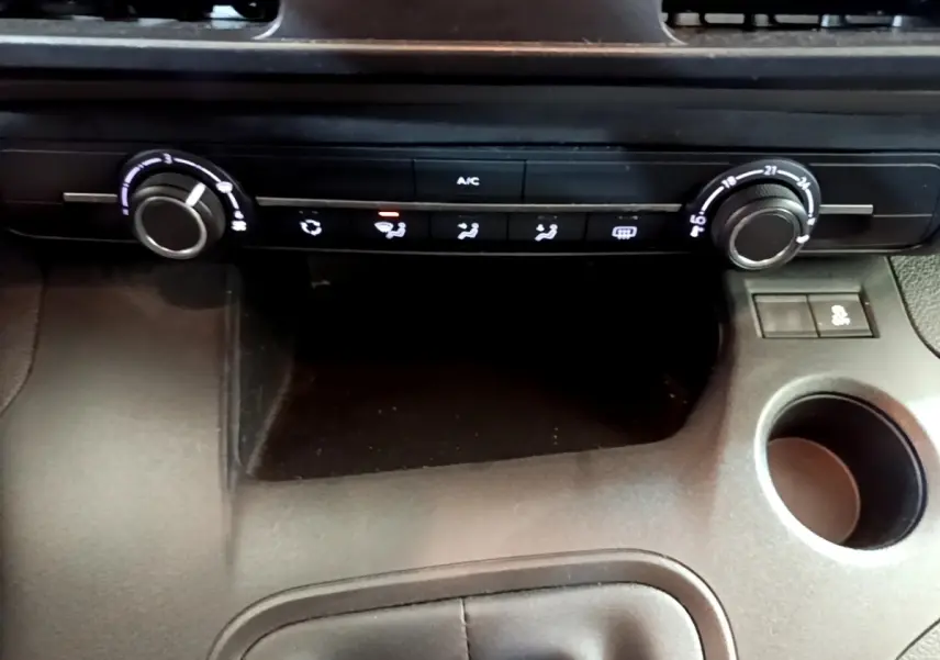 Vue rapprochée de la console centrale du Peugeot Rifter blanc, montrant les commandes de climatisation et un porte-gobelet.