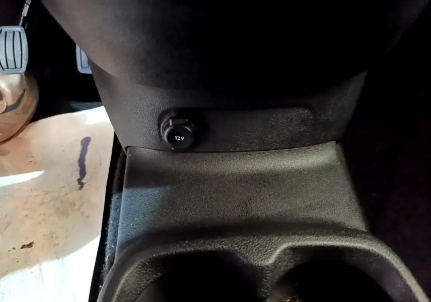 Prise 12V en gros plan sur la console centrale avant du Peugeot Rifter blanc, côté conducteur.