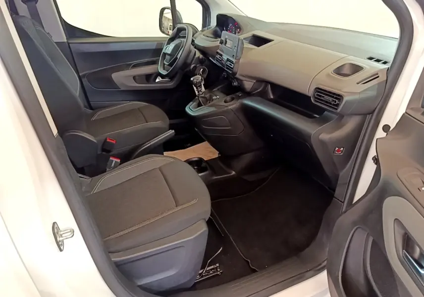 Vue intérieure côté conducteur du Peugeot Rifter blanc 2019, montrant tableau de bord, volant et sièges tissu noirs.